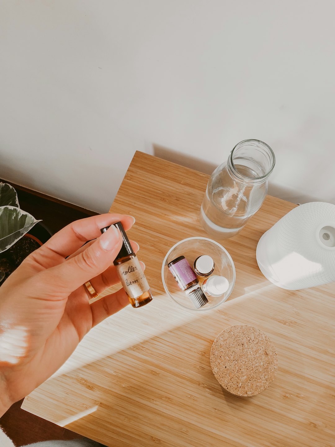A hand holds an essential oil bottle over a wooden table.